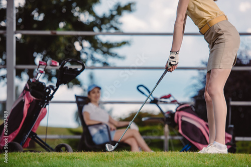 partial view of female golf player playing golf while friend resting behind at golf course