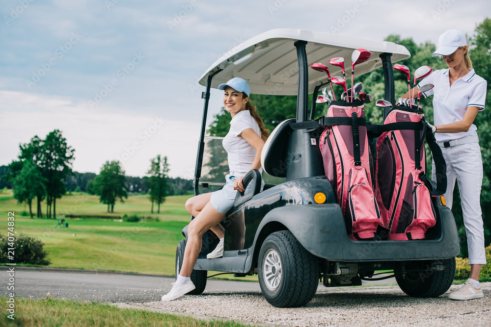 smiling female golf players at golf cart getting ready for game at golf course