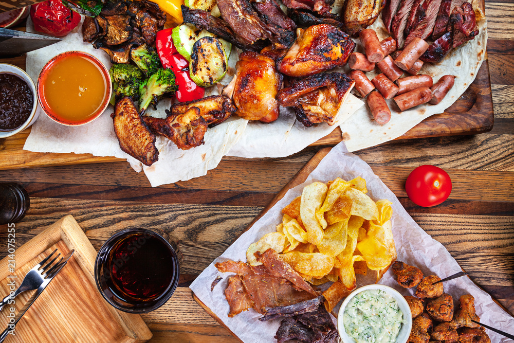 Grilled assorted food set on wooden background. Top view dishes of grilled chicken, potato, cola, sausage. Grilled assorted food set on wooden background. Top view dishes of grilled chicken, potato, cola, sausage.