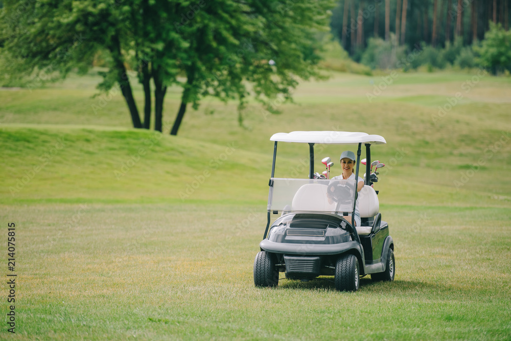 Woman in cap riding golf cart at golf course on summer day