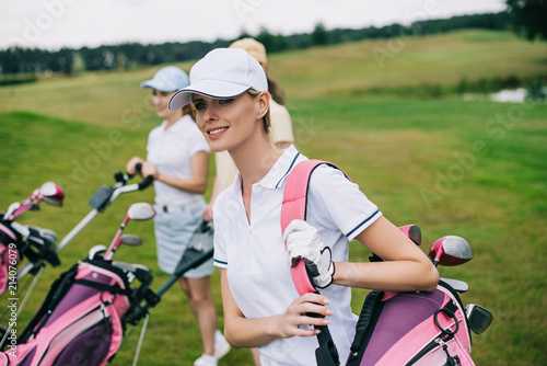 smiling women in caps with golf equipment on golf course
