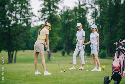Woman in cap playing golf while smiling friends standing near by at golf course
