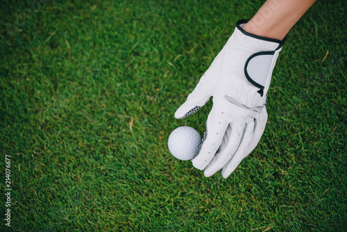 Partial view of woman in golf glove putting ball on green lawn at golf course