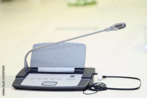 A row of microphone and headphone sets for speech and translation on a business or congress meeting on a desk. Translation booths are seen in the background.