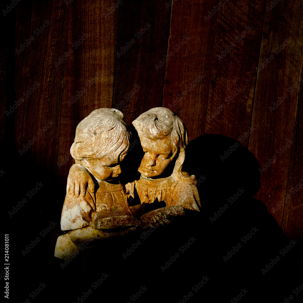 Two girls statues reading book against wood panelled wall