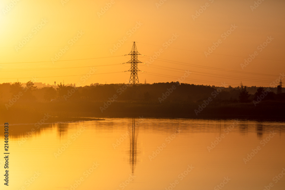 Electric pillar with reflection in the water at sunset