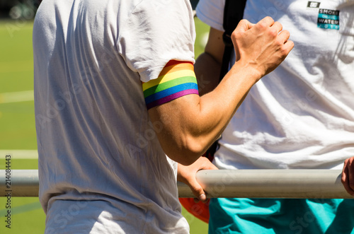 Midsection of Man Wearing White Shirt and LGBT Band Touching Gray Metal Pole while Standing at Soccer Field