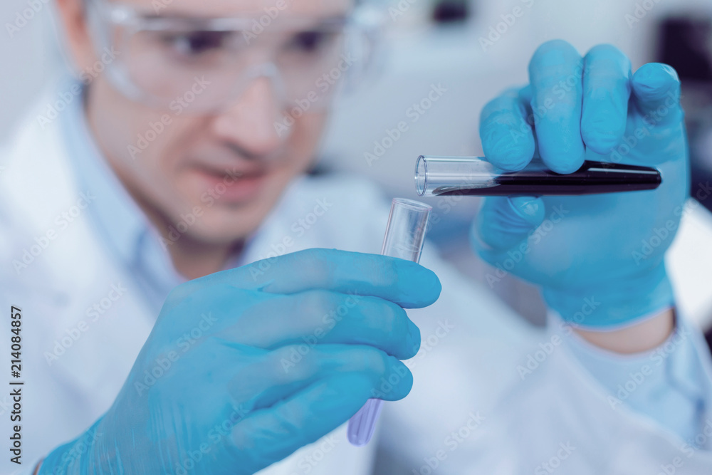 Scientific studies. Selective focus of a test tube with dark blue liquid in it being poured into another test tube Scientific studies. Selective focus of a test tube with dark blue liquid in it being poured into another test tube