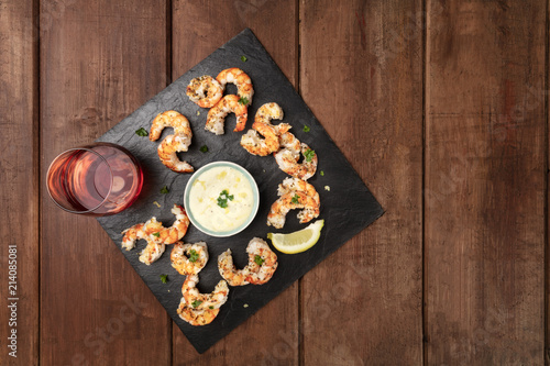 Overhead photo of shrimps on a dark rustic background, with a sauce and a glass of rose wine, with place for text