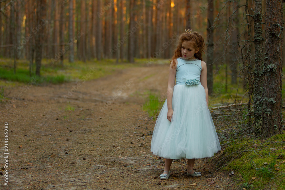 Little emotional girl walks in a summer forest in a dress