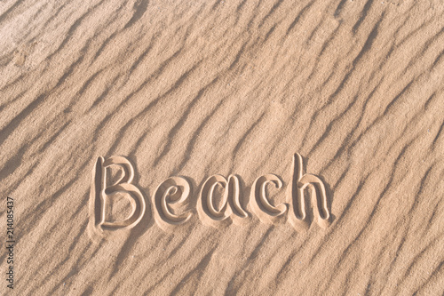 The word beach is written on the sand by hand. Beach season. Postcard. Shadows on the sand.