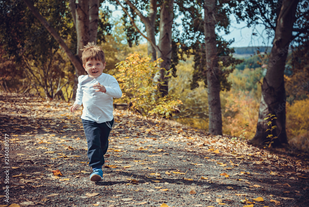 Cute smiling boy running in autumn park Cute smiling boy running in autumn park