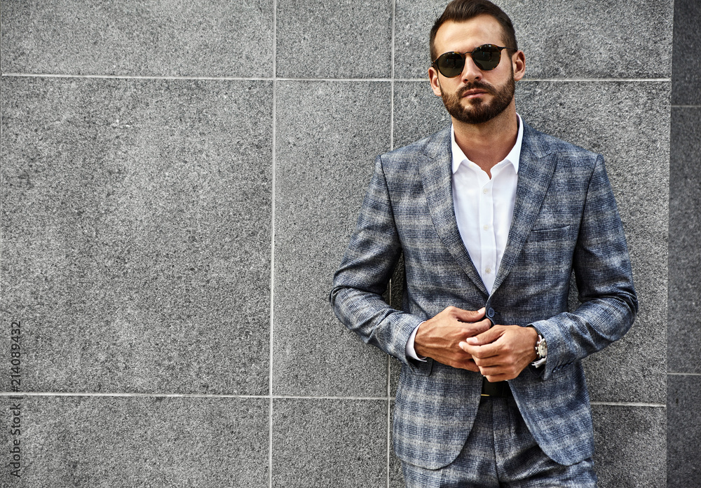 Portrait of sexy handsome fashion businessman model dressed in elegant checkered suit posing near gray wall on street background. Metrosexual Portrait of sexy handsome fashion businessman model dressed in elegant checkered suit posing near gray wall on street background. Metrosexual