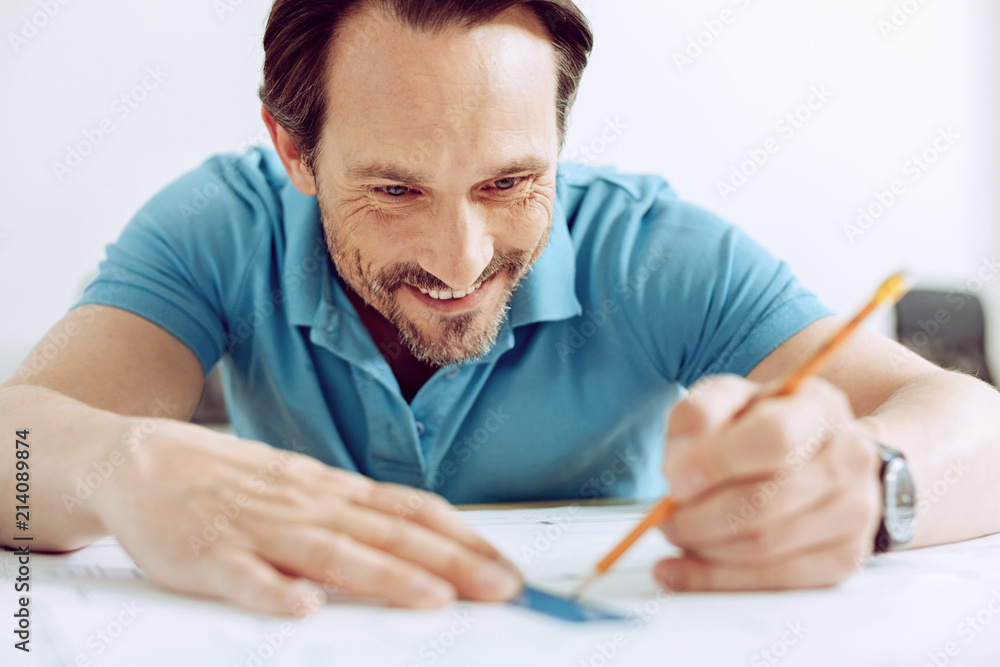 Easy work. Experienced young smiling engineer drawing the lines while finishing his project Easy work. Experienced young smiling engineer drawing the lines while finishing his project