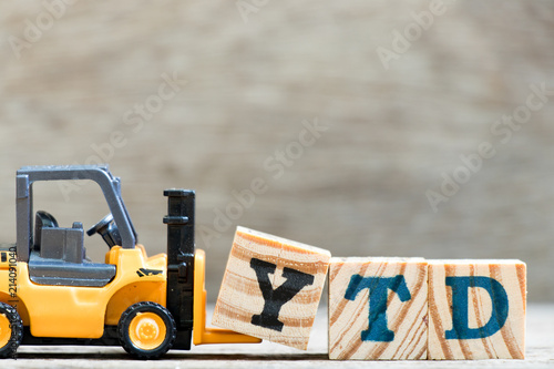 Toy forklift hold letter block Y in word YTD (abbreviation of year to date) on wood background photo