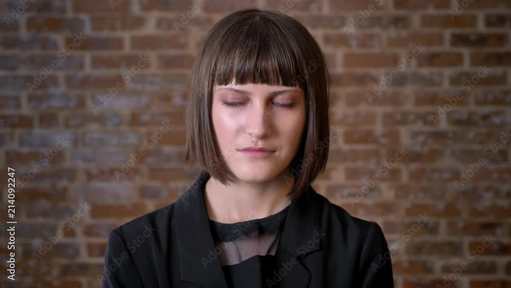 Young woman standing near brick wall and looking at camera and sideways Young woman standing near brick wall and looking at camera and sideways