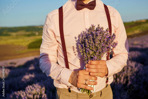 Close-up of a bouquet of lavender in the hands of the groom in the field of lavender.