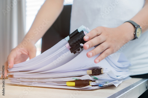 Business Documents concept : Employee woman hands working in Stacks paper files for searching and checking unfinished document achieves on folders papers at busy work desk office. Soft focus