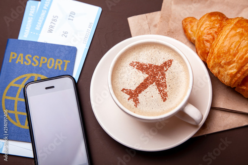 Mug of coffee with an airplane on the foam. Morning coffee with croissant in flight. Paspor and ticket with smrtrfonom
