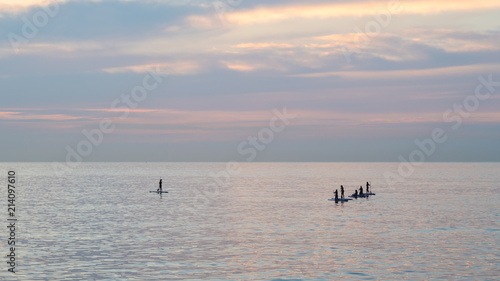 Team of young women standing up on a paddle surf board, enjoying a beautiful sunrise on the ocean