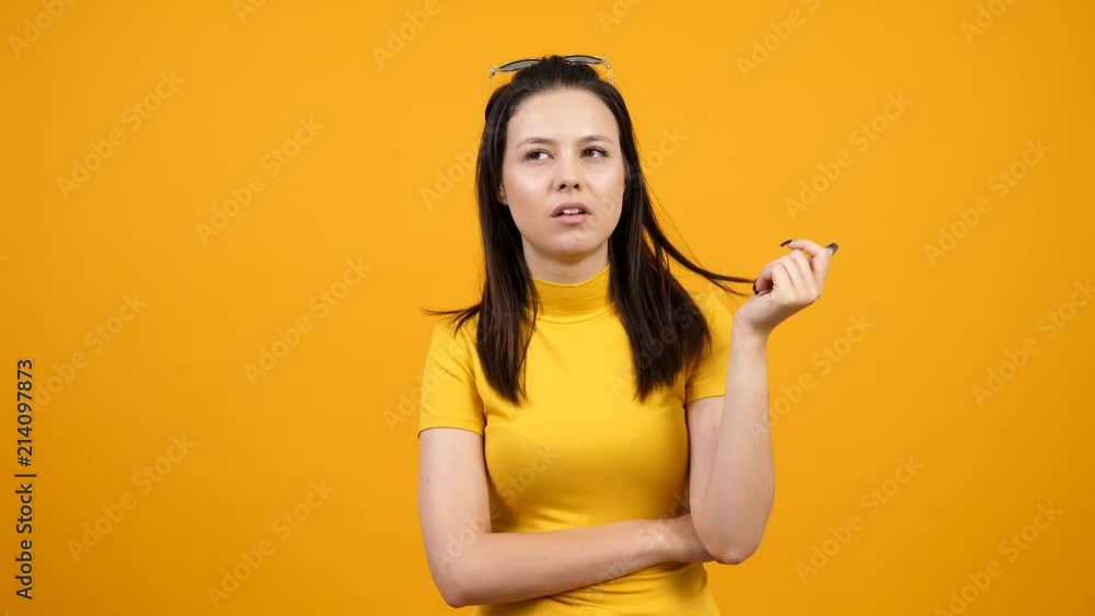Bored girl chewing gum on vivid orange background in studio. Arrogant teenager girl playing with her hair. Slow motion footage Bored girl chewing gum on vivid orange background in studio. Arrogant teenager girl playing with her hair. Slow motion footage