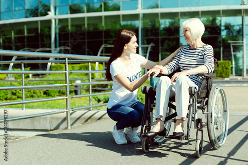 Young volunteer. Kind brunette sitting in semi position while supporting old female and expressing positivity photo