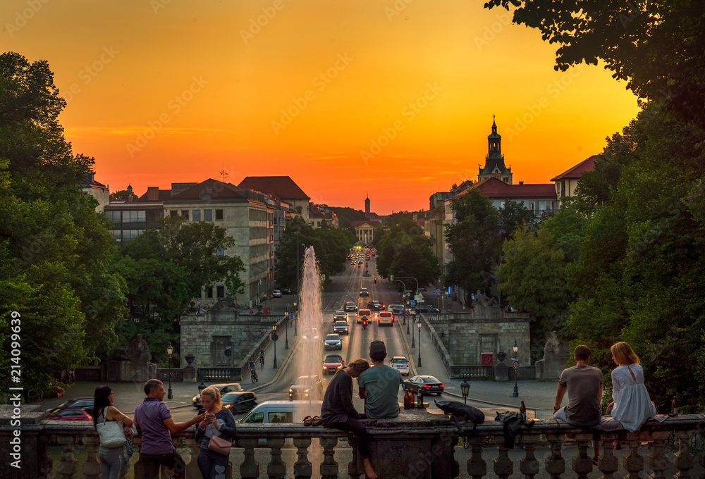 Naklejka premium München bei Nacht - Blick auf die gut befahrene Prinzregentenstraße bei tollem Licht mit glücklichen Paaren im Vordergrund, die den goldenen Sonnenuntergang über der Stadt genießen