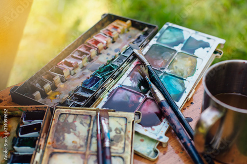Palette of watercolor paints and brushes on the wooden background.