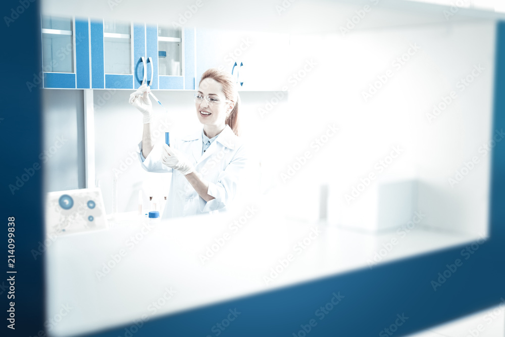 At the lab. Professional nice female scientist standing in the lab and wearing protective equipment while doing a scientific experiment At the lab. Professional nice female scientist standing in the lab and wearing protective equipment while doing a scientific experiment