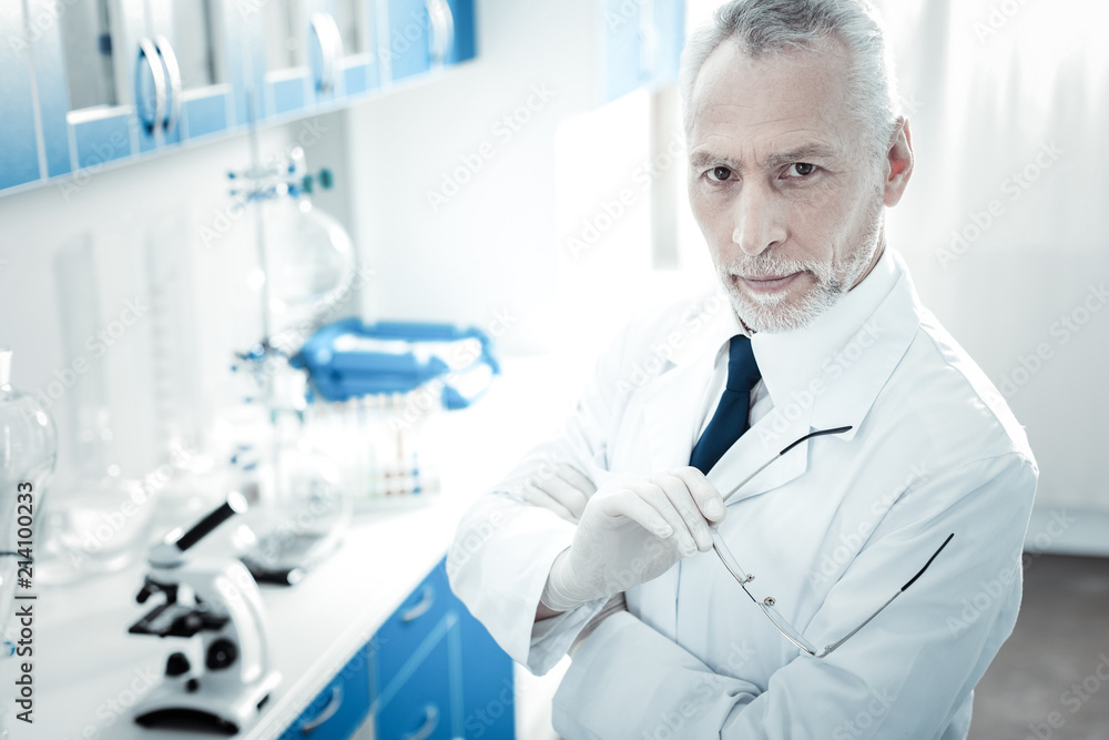 True professional. Handsome smart professional scientist holding his glasses and looking at you while standing in the lab True professional. Handsome smart professional scientist holding his glasses and looking at you while standing in the lab