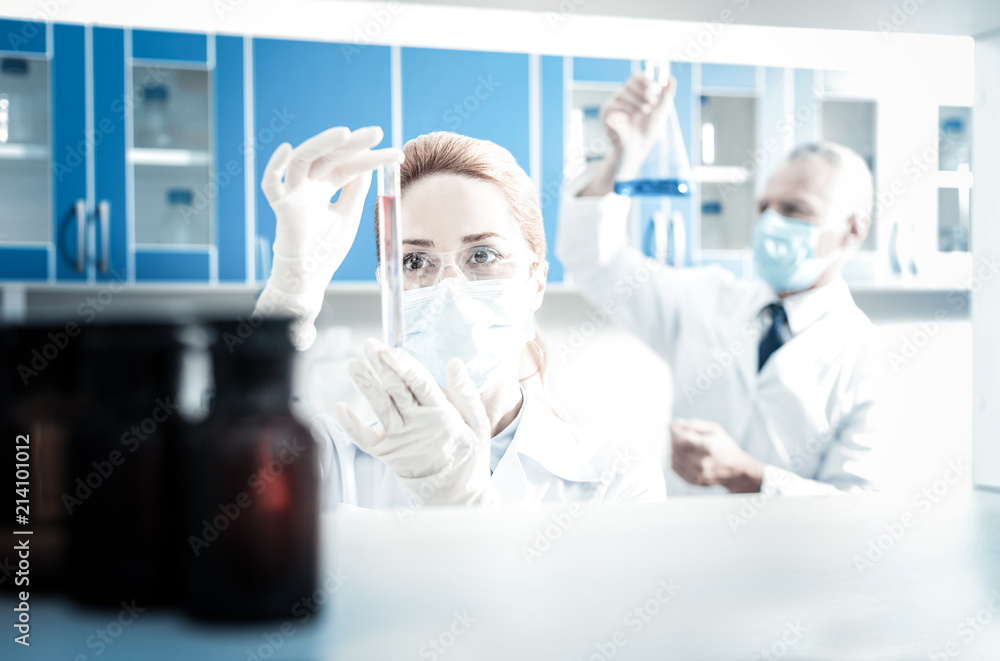 Laboratory research. Serious nice female researcher wearing protective equipment and holding a test tube while doing laboratory research Laboratory research. Serious nice female researcher wearing protective equipment and holding a test tube while doing laboratory research