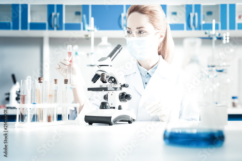 Scientific studies. Smart experienced nice biologist sitting in front of the microscope and wearing protective equipment while doing an analysis