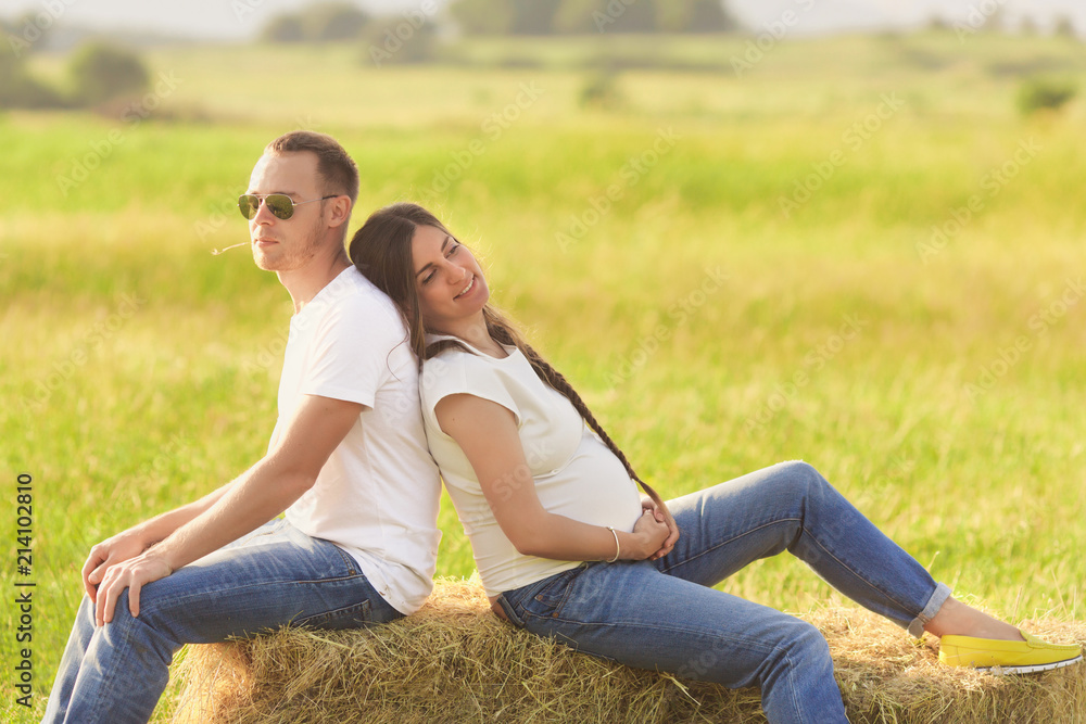Young pregnant woman with her husband enjoying the nature wearing casual and style jeans and white t-shirt. Young pregnant woman with her husband enjoying the nature wearing casual and style jeans and white t-shirt.