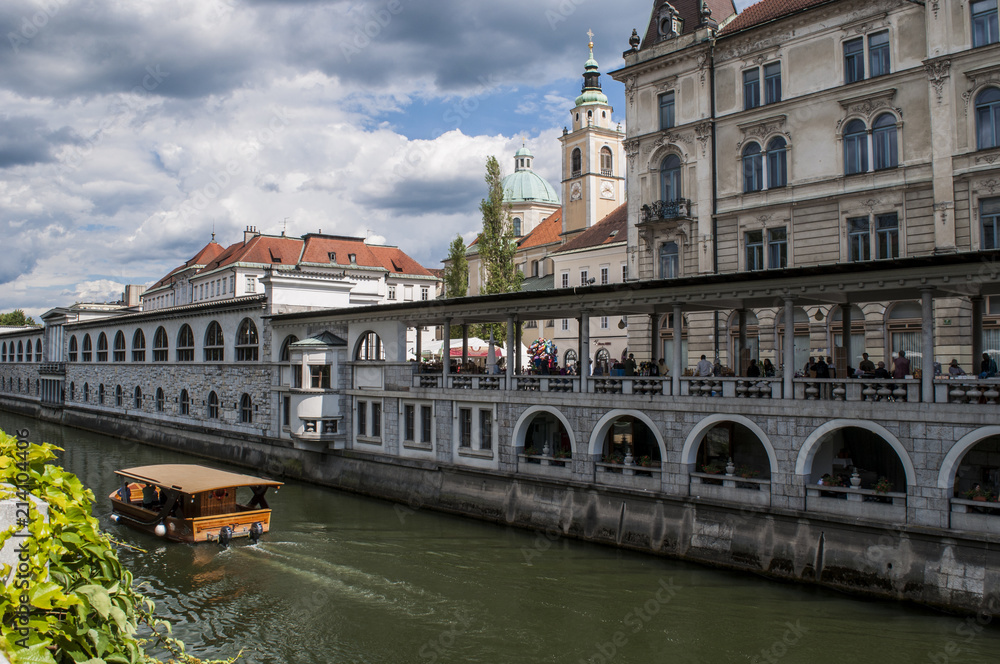 Obraz premium Slovenia, 24/06/2018: vista dello skyline del centro di Lubiana, la capitale slovena, con una barca turistica in navigazione naviga sul fiume Ljubljanica