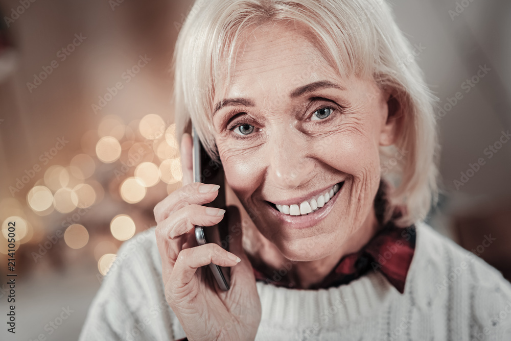Waiting for you. Attractive woman keeping smile on her face and holding gadget near ear while looking at camera Waiting for you. Attractive woman keeping smile on her face and holding gadget near ear while looking at camera