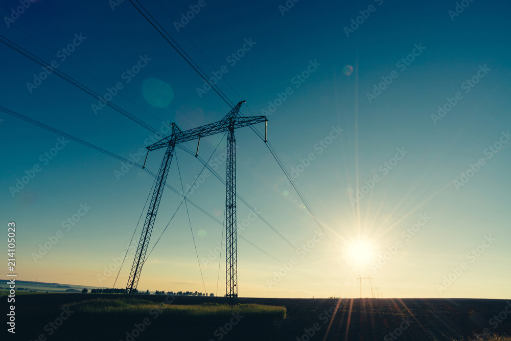 Power lines on background of blue clear sky in backlight from sunlight close-up. Silhouette of electric tower against of sun with copy space. Wires of high voltage above ground. Electricity industry.
