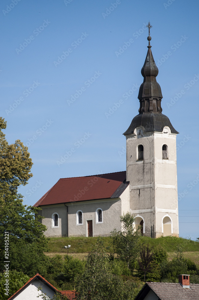 Slovenia: uno dei tipici villaggi sloveni con la chiesa parrocchiale sulla cima di una collina, i prati verdi prati e i terreni coltivati in campagna