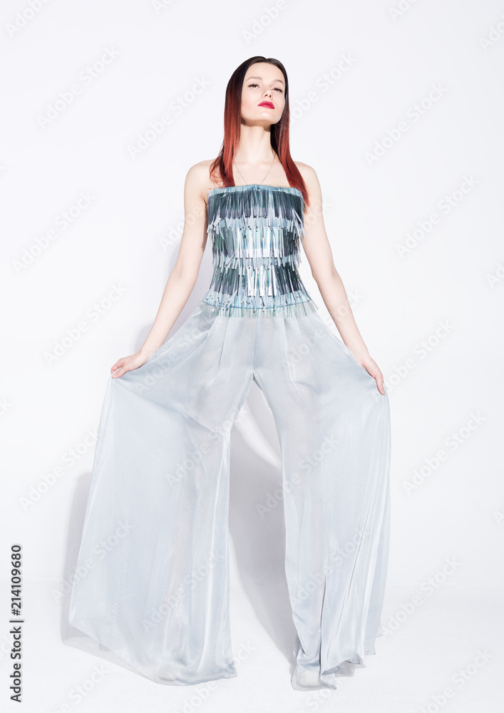 Fashion model posing in a silver suit with wide pants on white background