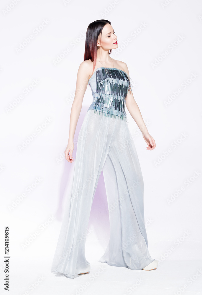 Fashion model posing in a silver suit with wide pants on white background.