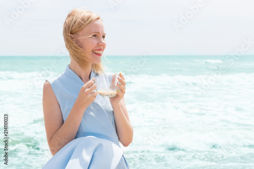 A woman is drinking tea with milk from a large cup on the ocean, the sea.
