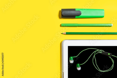 line of business or education accessories. green pencils, headphones, paper stickers, markers and tablet pc lying on a yellow surface. concept of the office chancery and gadgets. free copyspace