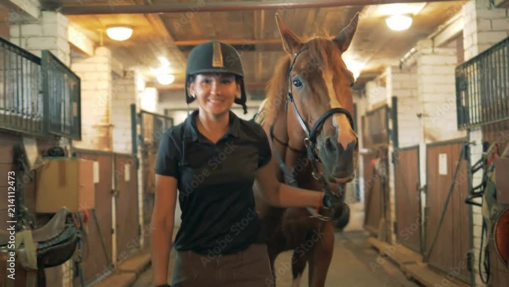Female rider smiles at camera in a stable, close up. Horsewoman portrait. Female rider smiles at camera in a stable, close up. Horsewoman portrait.