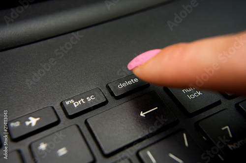 Female finger presses delete button on black laptop