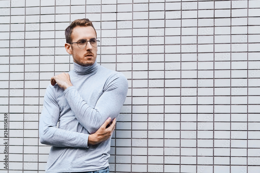 Hipster wearing glasses, standing near the wall made of small tiles Hipster wearing glasses, standing near the wall made of small tiles