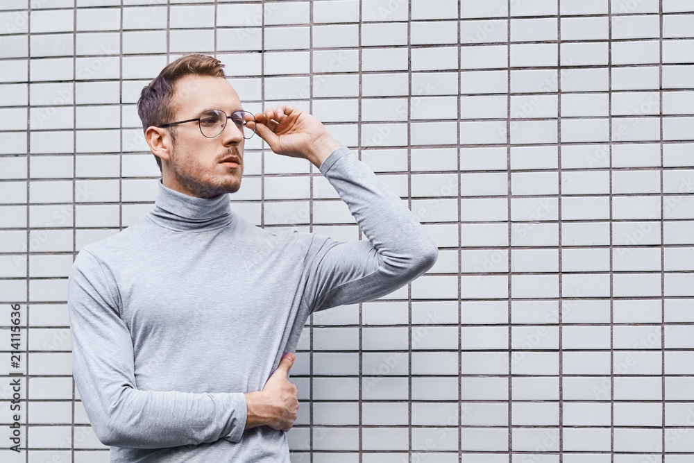 Hipster wearing glasses, standing near the wall made of small tiles Hipster wearing glasses, standing near the wall made of small tiles