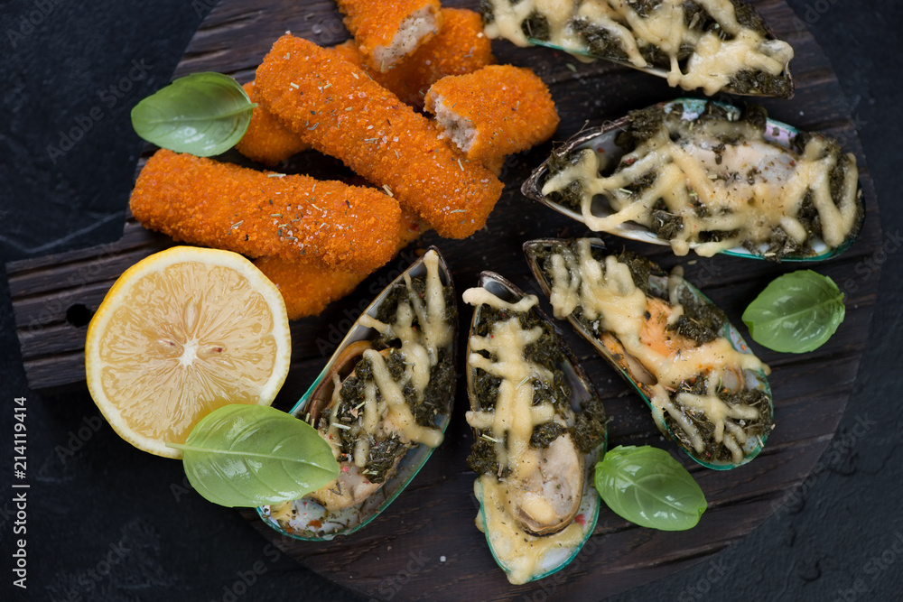Above view of mussels baked with spinach and cheese and roasted fish fingers on a wooden serving board, closeup