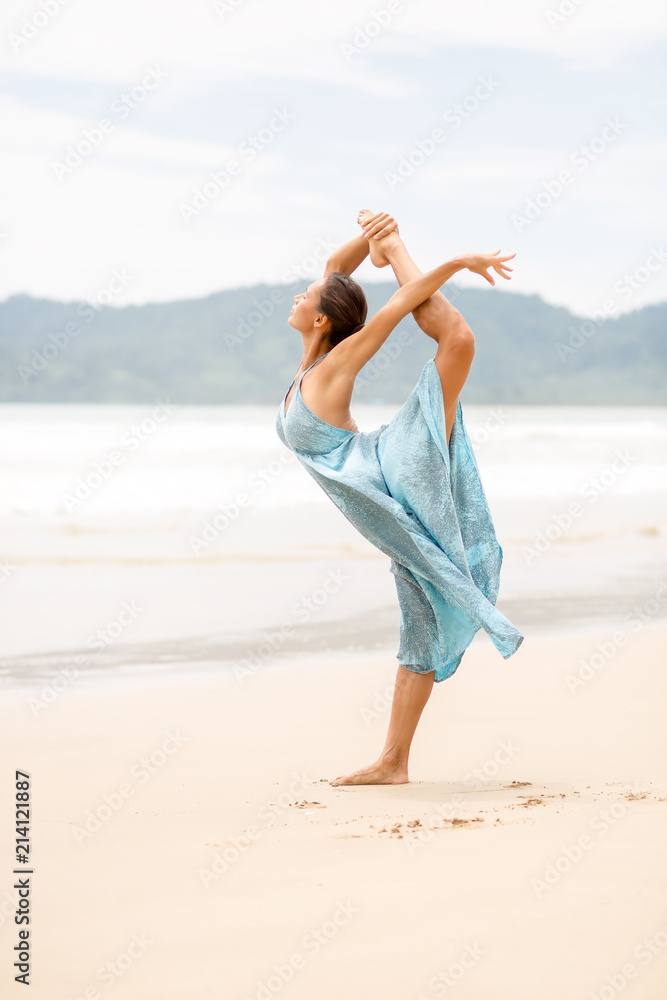 Fashion photo of young woman in long blue dress doing stand split leap. Amazing beach style girl, windy hair, toned, sugaring legs, beach wear, tender skin. Summer day and happy holiday concept. Fashion photo of young woman in long blue dress doing stand split leap. Amazing beach style girl, windy hair, toned, sugaring legs, beach wear, tender skin. Summer day and happy holiday concept.