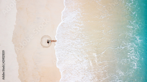 Aerial view of young woman in blue bikini making sand angel. Hot beach with cool waves. Summer and holiday concept, seascape with girl, beach, beautiful waves, blue water. Top view from drone shot.