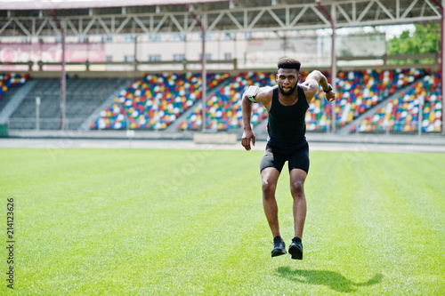 African american male athlete in sportswear doing jump exercise at stadium.