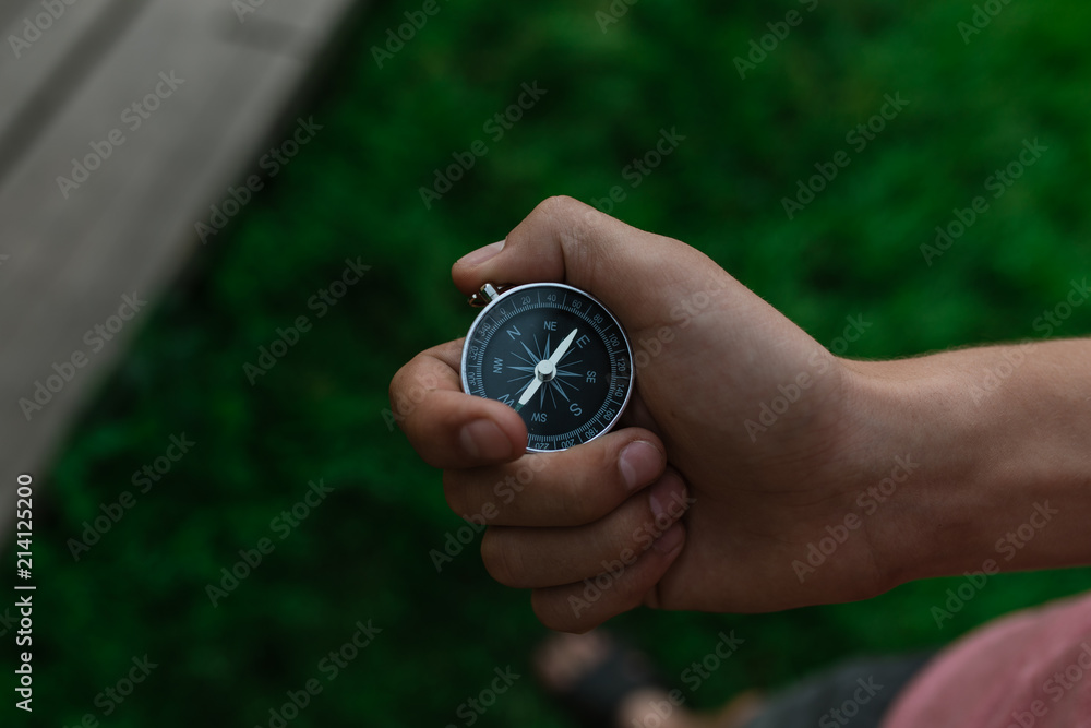 A traveler with a compass in the park. A compass in hand against a background of a blurred road. The direction of finding tourists with a compass in the forest. to get lost in the forest. A traveler with a compass in the park. A compass in hand against a background of a blurred road. The direction of finding tourists with a compass in the forest. to get lost in the forest.